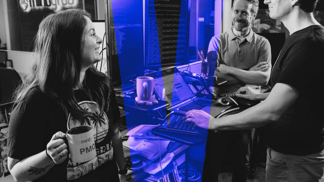 Three employees laugh around a standing desk with a purple V graphic overlay